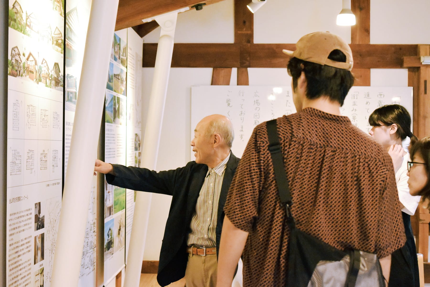 資料館のような場所で展示を指さしながら説明する地域の人とそれを聞く参加者