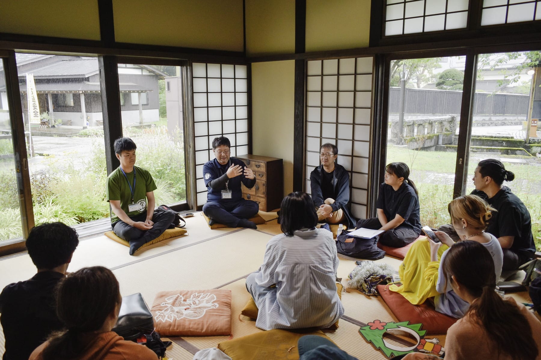 民家の和室に集まり、役場の人の話を聞く参加者