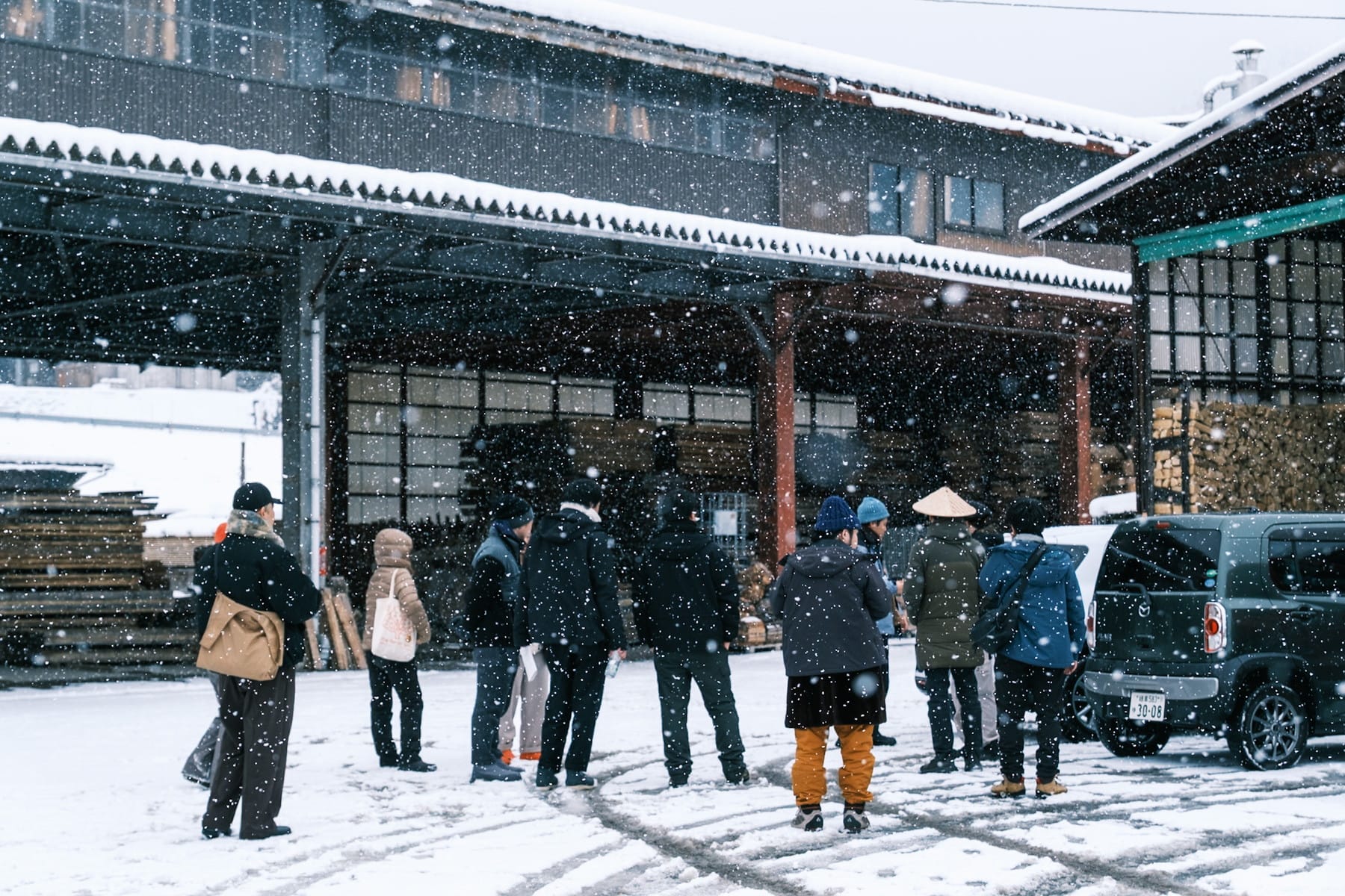 雪が降る中、製材所の前で話を聞く参加者